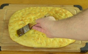 brushing cooled focaccia with olive oil