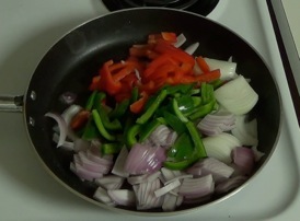 adding onions and peppers to frying pan